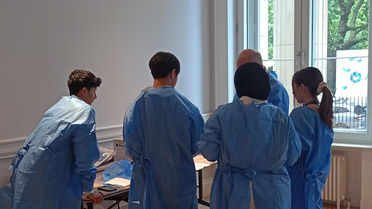 Five individuals, facing away from the camera, wearing blue surgical gowns.