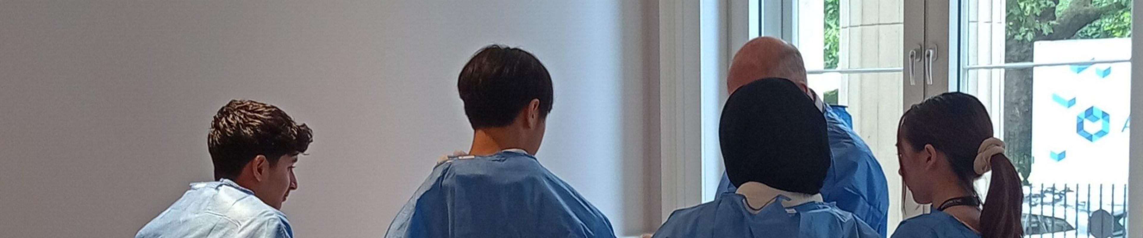 Five individuals, facing away from the camera, wearing blue surgical gowns.