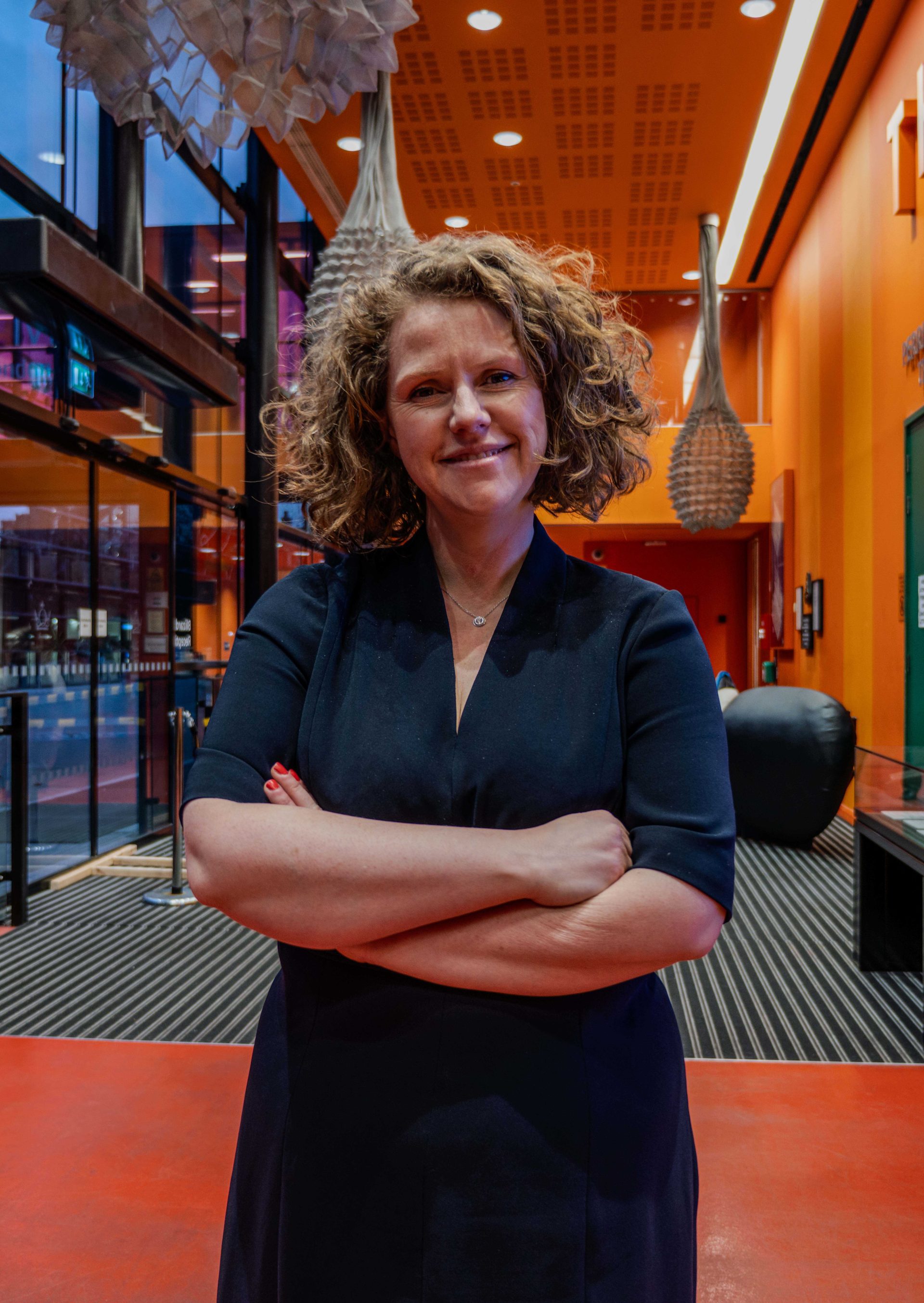 Individual in a black dress, standing in a building atrium with orange walls