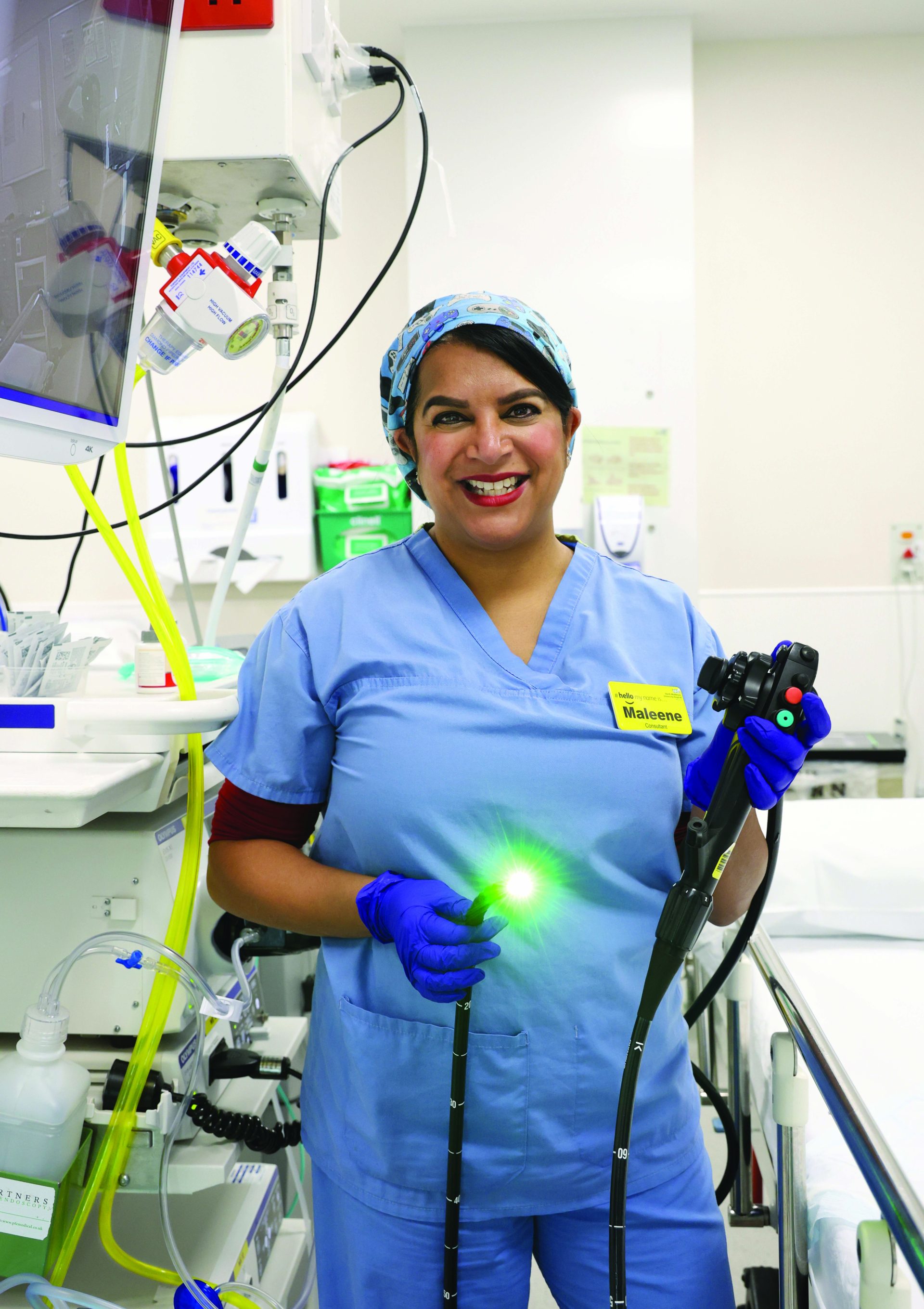 Individual in blue scrubs, standing in a clinical room holding an endoscope
