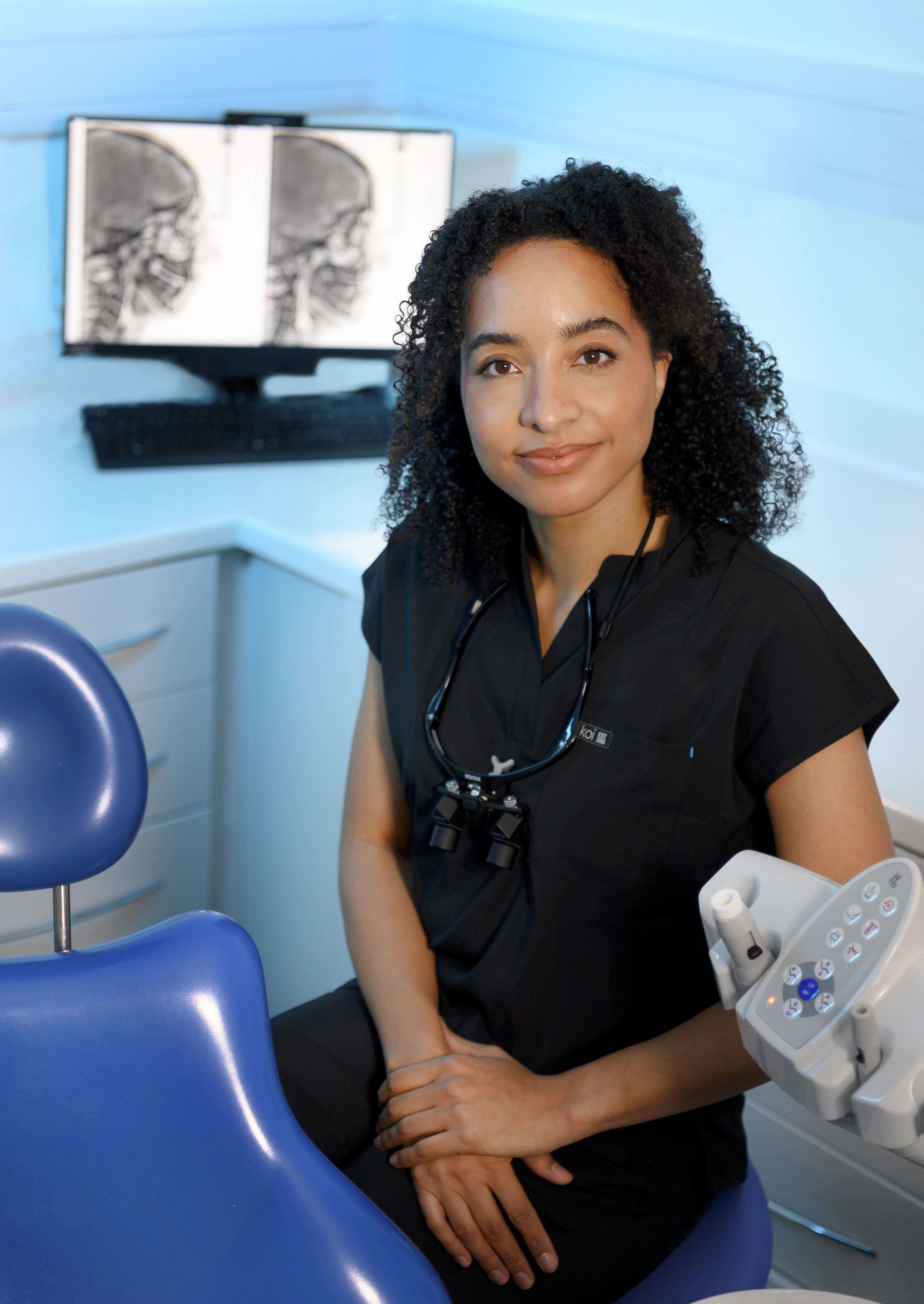 Individual in black scrubs, sitting in a dental clinical room