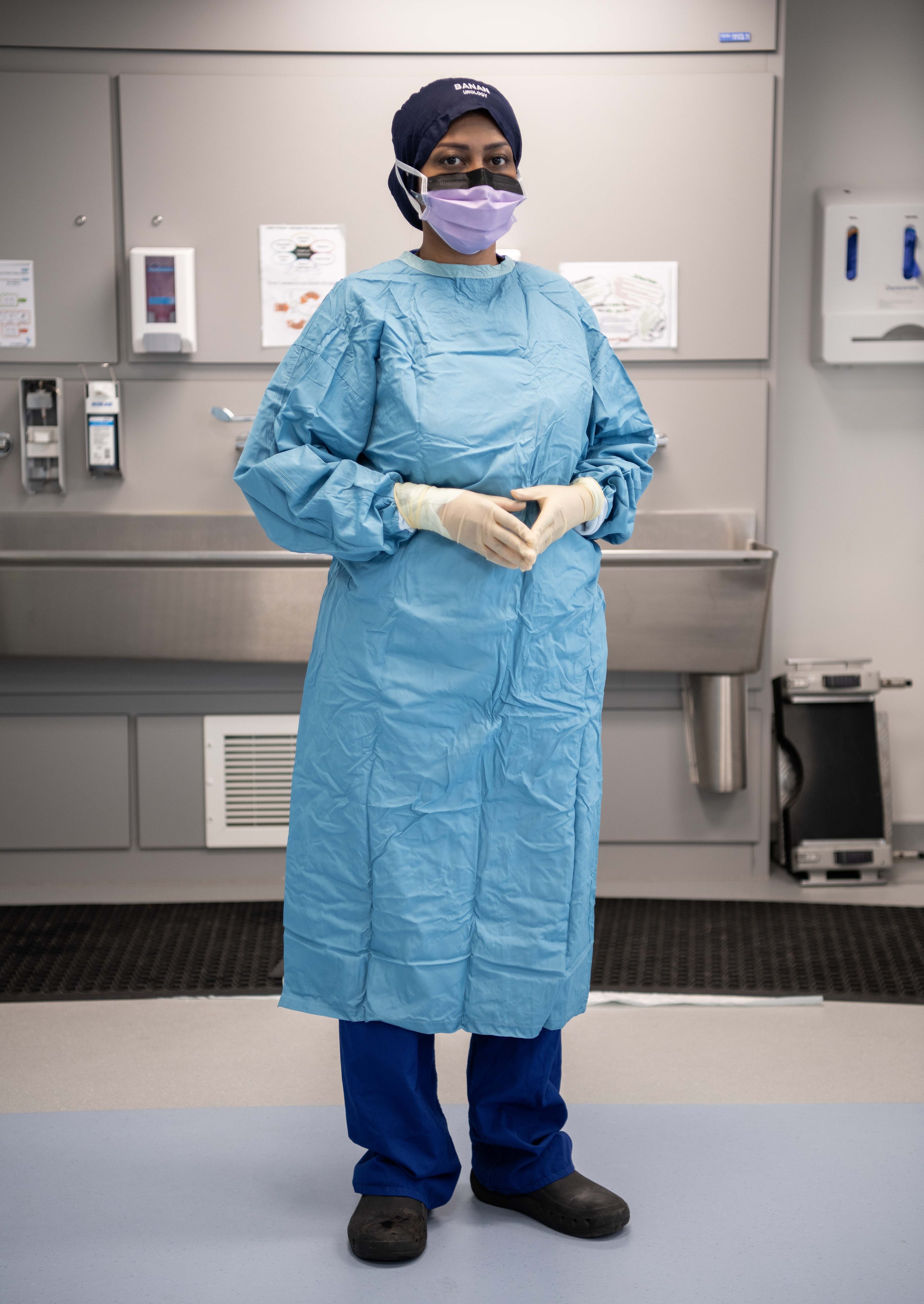 Individual in surgical gown, gloves and mask, standing in a scrub room in front of a sink
