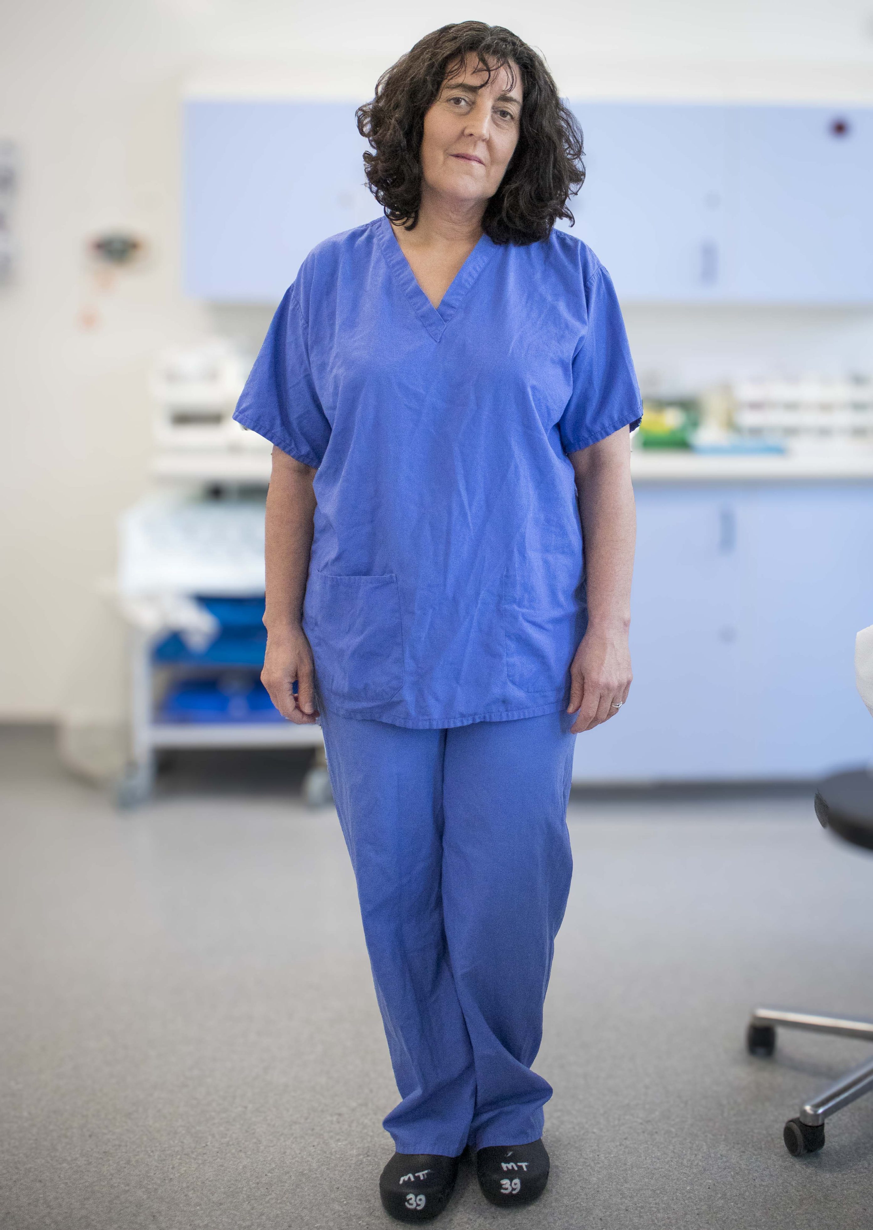 Individual wearing blue scrubs standing in a clinical room